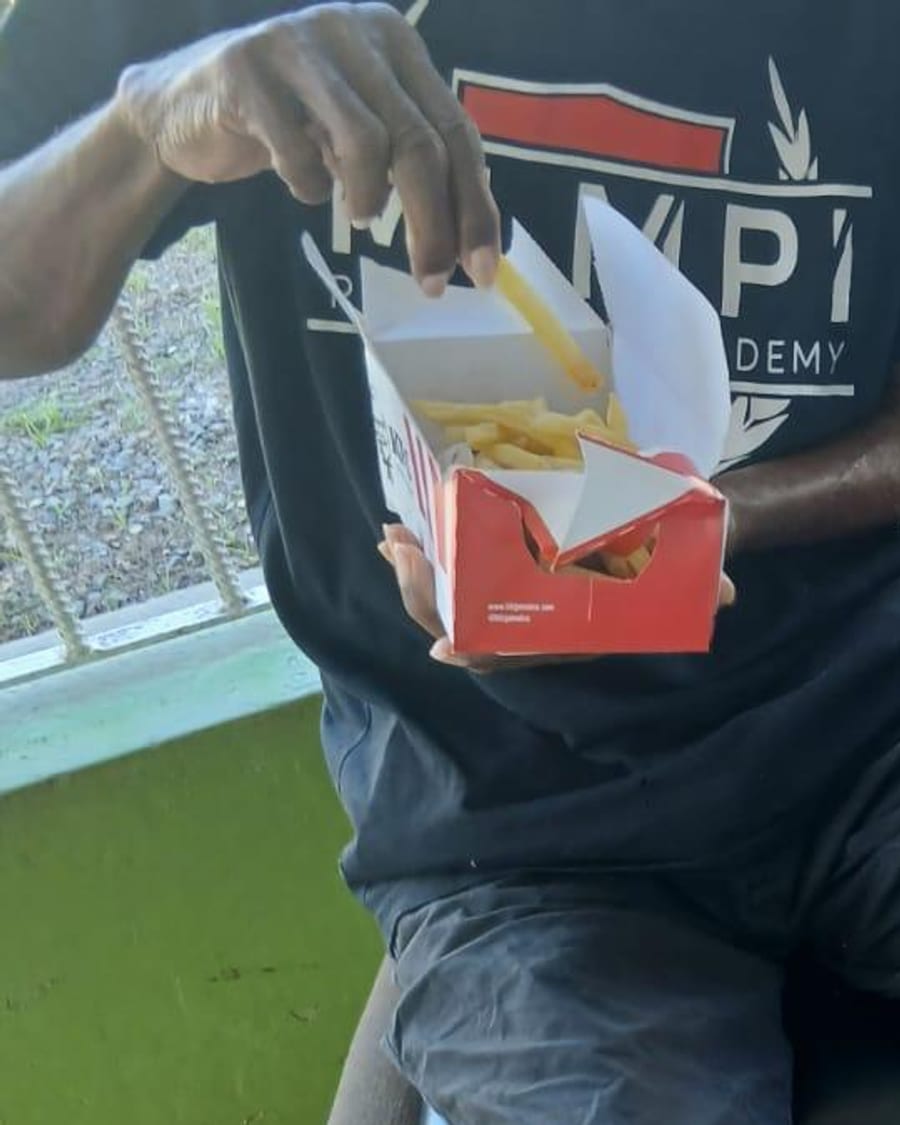 An elderly man eating a hot meal from a takeaway box, held in his lap.